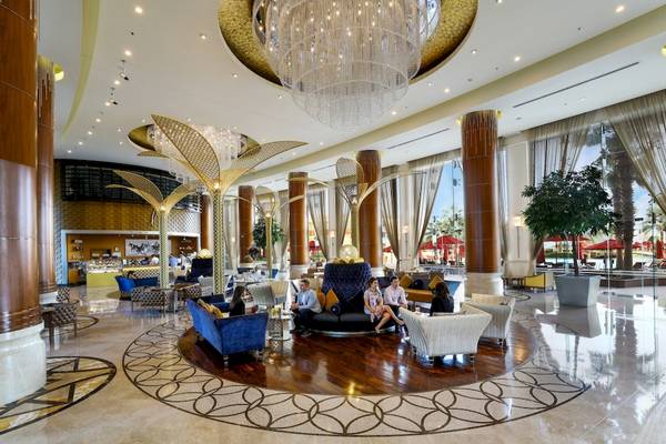 Lobby des Khalidiya Palace Rayhaan by Rotana mit kristallenem Kronleuchter und Gästen auf Sitzmöbeln.