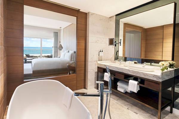 Badezimmer in einer Hotelsuite mit Blick auf das Meer, Bett und große Fenster.
