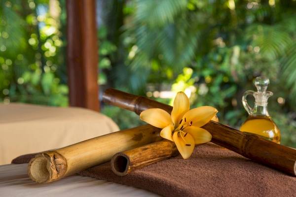Bambusrohre, eine gelbe Blume und ein Ölflakon auf einem Massagebett im Freien.