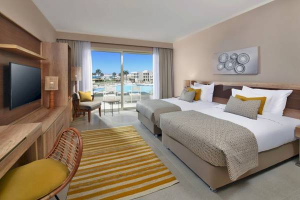 Doppelzimmer im Steigenberger Resort Ras Soma mit zwei Betten, Fernseher, Tisch und Aussicht auf den Pool.