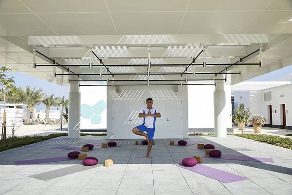Ein Mann praktiziert Yoga auf einer Terrasse im Riu Dubai, umgeben von Yogamatten und Meditationskissen.