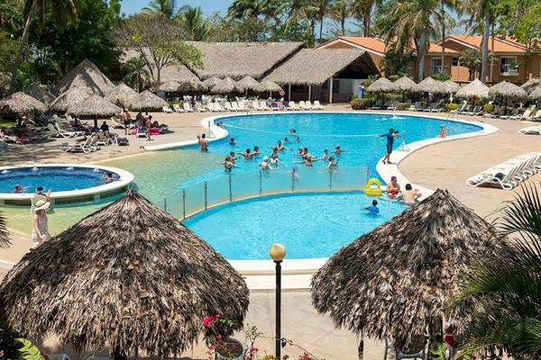 Gesamtansicht des Swimmingpool-Bereichs des Occidental Tamarindo Hotels mit vielen Gästen und Sonnenschirmen.