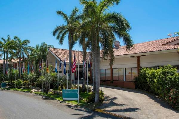 Eingangsbereich des Occidental Tamarindo Hotels mit Palmen und verschiedenen Flaggen
