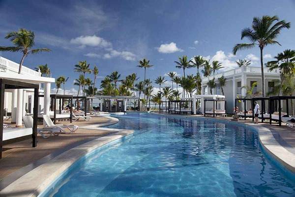 Außenpoolbereich des Riu Palace Bavaro Hotels mit weißen Liegestühlen und Palmen.