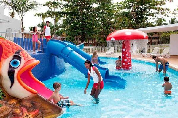Familien, die im Poolbereich des Riu Palace Bavaro spielen, mit Wasserrutschen und einer Wasserpilzskulptur.