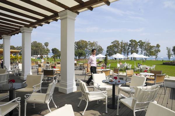 Außenterrasse des Louis Kerkyra Blue Hotels mit Gästen unter Sonnenschirmen und Blick auf einen Rasen und das Meer.