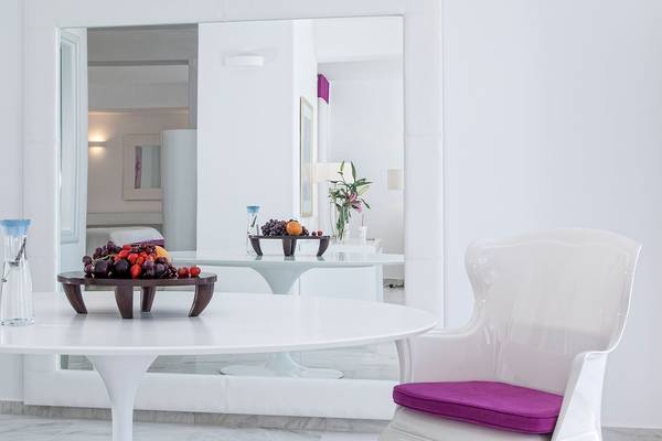 Ein elegantes weißes Esszimmer im DeLight Boutique Hotel mit Obst auf dem Tisch und einem Spiegel, der das Zimmer reflektiert.