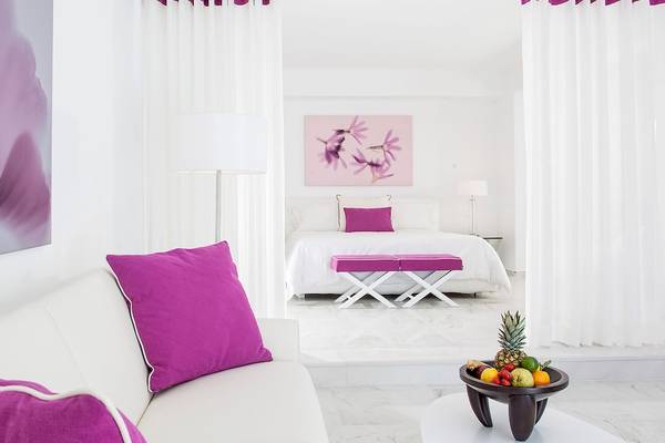 Weißes Zimmer mit violetten Akzenten, Bett, Sofa, Früchteschale auf Tisch im DeLight Boutique Hotel.