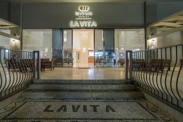 Außenansicht des Mitsis La Vita Beach Hotels mit beleuchtetem Logo und Eingangsbereich.