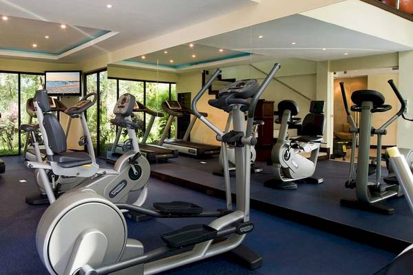 Fitnessstudio im Occidental Tamarindo Hotel mit verschiedenen Geräten und Blick auf Bäume.
