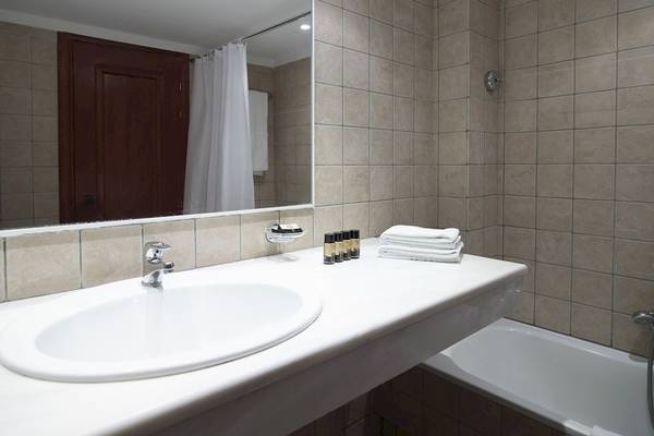 Badezimmer im Mitsis La Vita Beach Hotel mit Spiegel, Waschbecken und Badewanne.