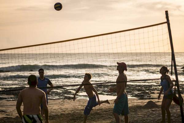 Gruppe von Menschen, die Volleyball auf einem Strand spielen, während die Sonne untergeht.
