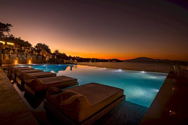 Nachtansicht des Pools im Alexandra Beach Resort & Spa mit illuminierten Liegen und einem beeindruckenden Sonnenuntergang im Hintergrund.