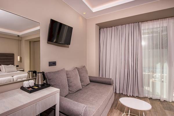Ein Hotelzimmer im Alexandra Beach Resort & Spa mit einem Bett, Spiegel, Fernseher, Sofa, Tisch und Fenstern.