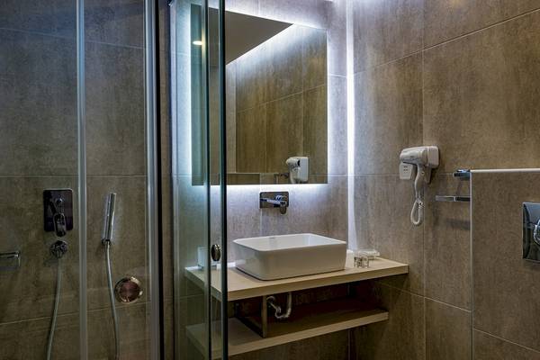 Badezimmer des Alexandra Beach Resort & Spa mit einer Glasdusche, einem Waschbecken und einem Föhn.