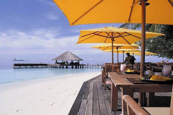 Restaurant am Strand des Dhawa Ihuru Hotels mit gelben Sonnenschirmen und Blick aufs Meer.