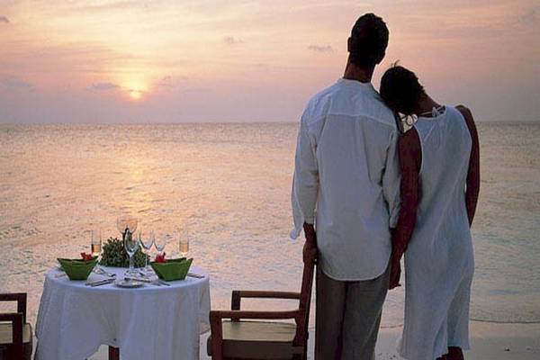 Ein Paar steht am Strand und genießt den Sonnenuntergang im Dhawa Ihuru Hotel.