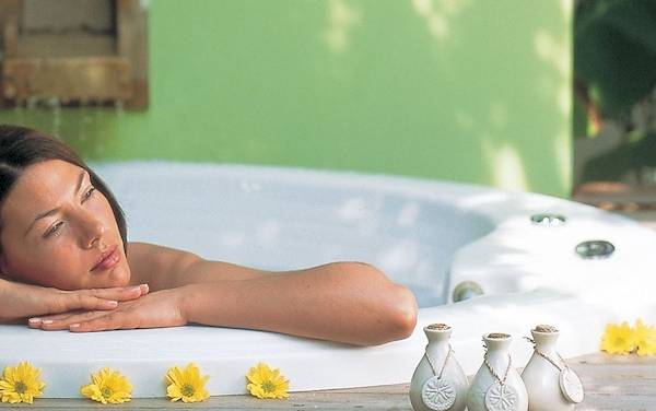 Eine Frau entspannt sich im Whirlpool im Dhawa Ihuru Hotel, umgeben von weißen Handtüchern und Blumen.