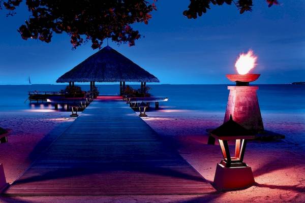 Dhawa Ihuru Strand bei Nacht mit einem beleuchteten Pfad und zwei Fackeln.