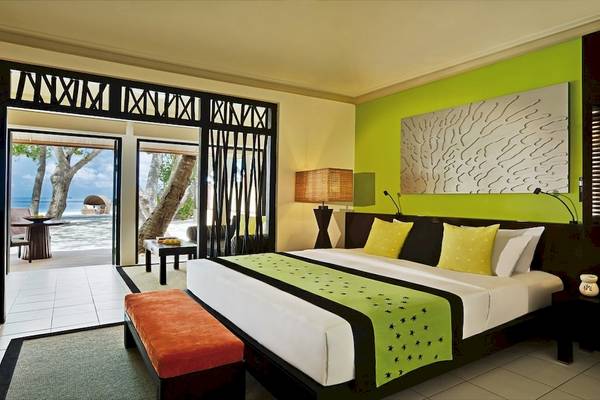 Schlafzimmer im Dhawa Ihuru Hotel mit grünen Wänden, einem großen Bett, und einer Terrasse mit Blick auf den Ozean.