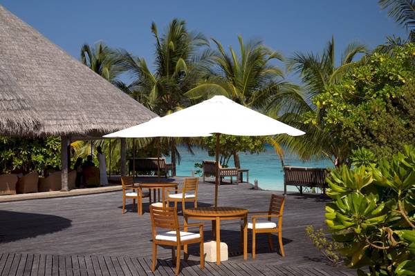 Terrasse des Coco Palm Dhuni Kolhu Hotels mit Tischen und Sonnenschirmen am Meer
