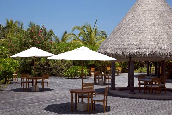 Außenbereich des Coco Palm Dhuni Kolhu Hotels mit Tischen, Stühlen und Sonnenschirmen.