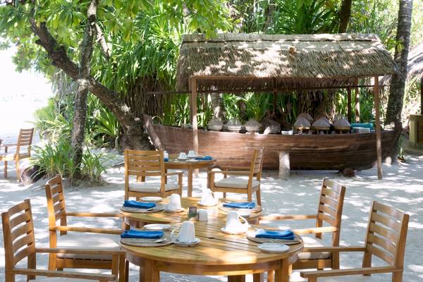 Outdoor-Essbereich im Coco Palm Dhuni Kolhu Hotel mit runden Tischen und Stühlen.