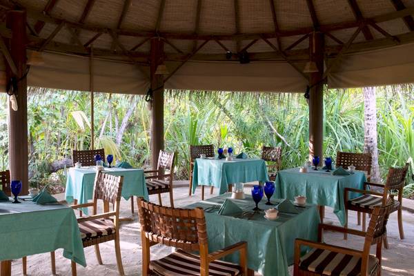 Gartenrestaurant des Coco Palm Dhuni Kolhu mit gedeckten Tischen und Stühlen.