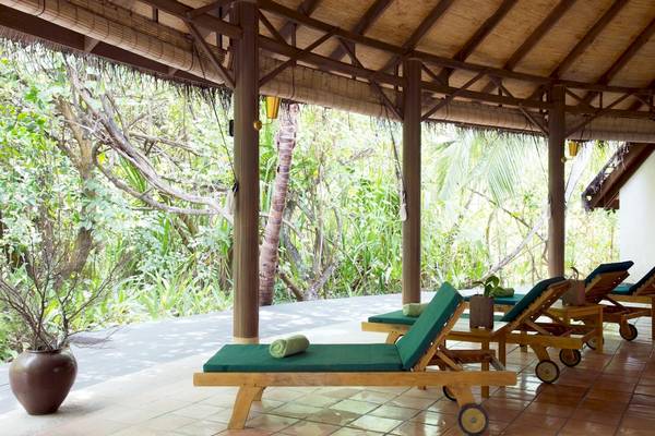 Coco Palm Dhuni Kolhu Hotel Terrasse mit grünen Loungesesseln und Blick auf den Wald.