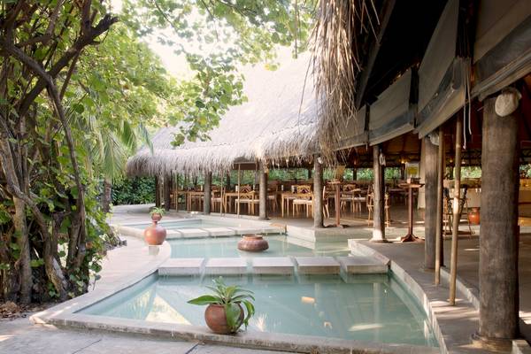 Außenbereich des Coco Palm Dhuni Kolhu Hotels mit einem Pool und einem gedeckten Essbereich.