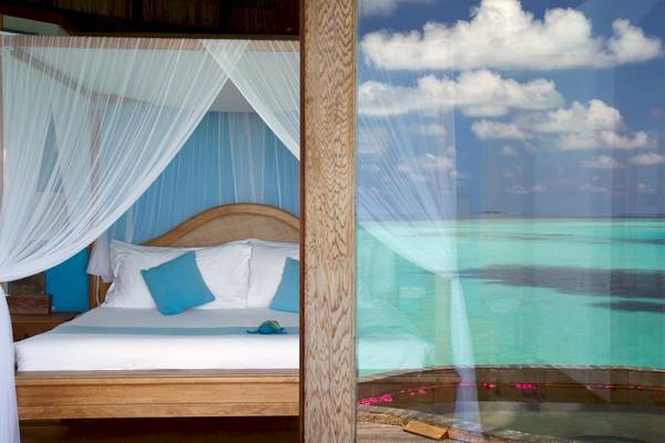 Zimmer im Coco Palm Dhuni Kolhu Hotel mit einem Bett, blauen Kissen und Meerblick.