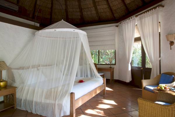 Schlafzimmer im Coco Palm Dhuni Kolhu Hotel mit Moskitonetz, weißen Vorhängen und Möbeln.