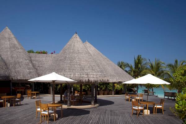 Außenterrasse des Coco Palm Dhuni Kolhu Hotels mit Tischen, Stühlen und Sonnenschirmen.