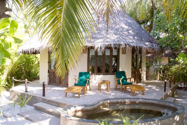 Coco Palm Dhuni Kolhu Ferienhaus mit zwei Liegen und einem kleinen Tisch auf der Veranda vor dem Haus.