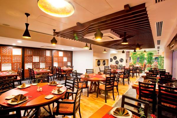 Innenansicht des Restaurants im Side Star Resort mit runden Tischen, Holzboden und stilvollen Deckenleuchten.