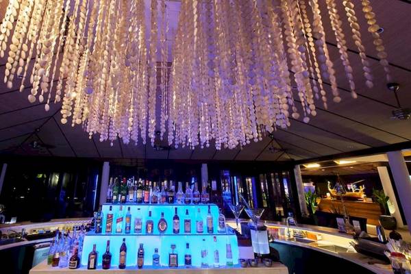 Bar im Lily Beach Resort & Spa mit einer großen, dekorativen Perlen-Chandeleir und einer Reihe von alkoholischen Getränken auf dem Regal.
