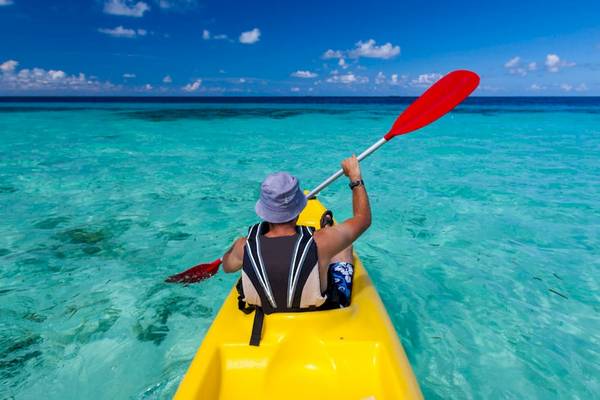 Ein Mann paddelt mit einem roten Paddel in einem gelben Kajak im Meer am Lily Beach Resort & Spa.