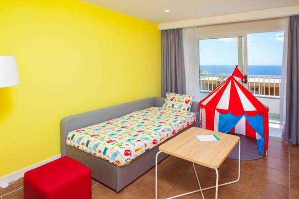 Zimmer im Abora Interclub Atlantic Hotel mit gelber Wand, Bett, Tisch, rotem Zirkuszelt und Balkon mit Meerblick.