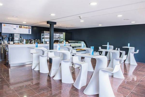 Innenbereich des Mogan Princess & Beach Club mit weißen Tischen und Stühlen, einer Theke und einer Anzeigetafel.