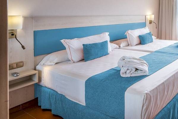 Doppelzimmer im Bluesea Costa Bastian Hotel mit zwei Betten, blauen Kissen, einer Nachttischlampe und einem Balkon.