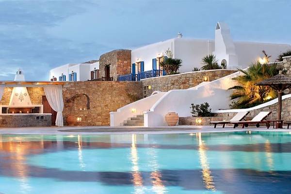 Abendansicht des Swimmingpools des Mykonos Grand Hotel & Resort mit Loungebereich und heller Beleuchtung.