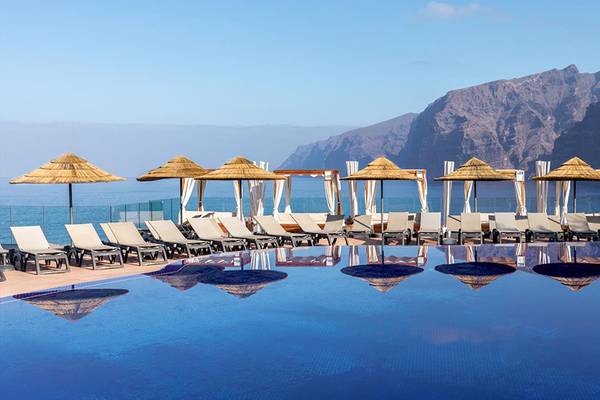 Ein Hotelpool mit Sonnenliegen, Sonnenschirmen und Blick auf die Berge.