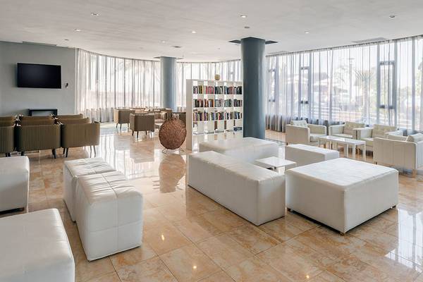 Hotellobby des Barcelo Santiago mit weißen Möbeln, Bücherregalen und großen Fenstern.