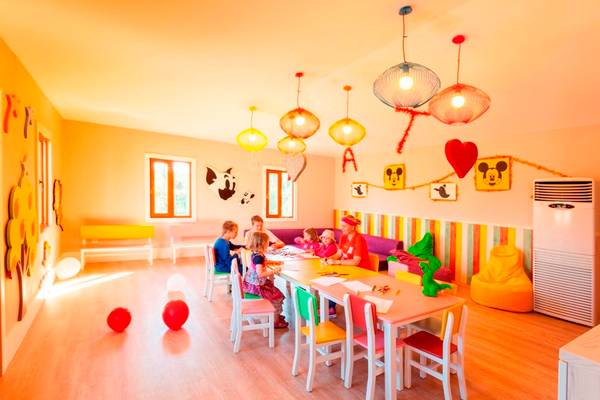 Gruppe von Kindern und Erwachsenen in einem farbenfrohen Raum des Side Star Resorts, mit bunten Stühlen, einem Tisch, dekorativen Lampen und einer bunt gestreiften Wand.