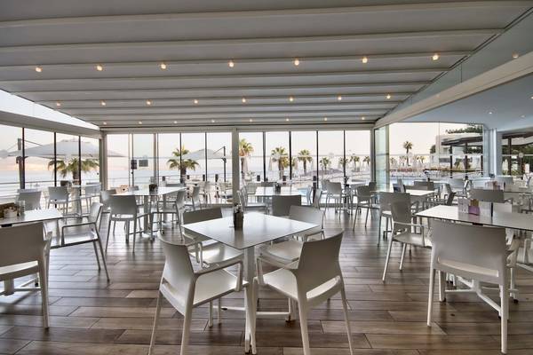 Innenansicht des Restaurants im Doubletree by Hilton Malta mit vielen weißen Tischen und Stühlen und einer Aussicht auf das Meer.