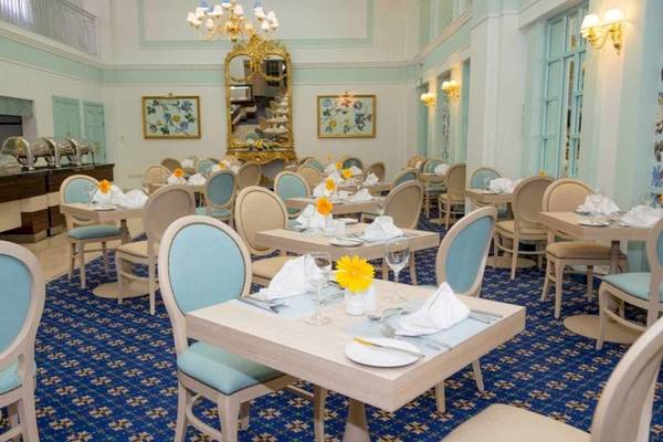 Speisesaal des AX The Victoria Hotels mit blauen Teppich, weißen und blauen Stühlen, Tischdecken und Blumengestecken.