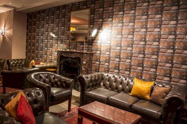Lobby des AX The Victoria Hotels mit Ledersofas, einem Kamin und büchertapetenbedeckten Wänden.