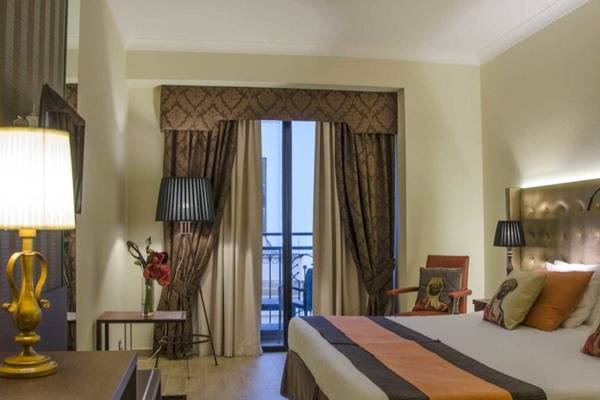 Zimmer im AX The Victoria Hotel mit Bett, Lampen und Balkon.
