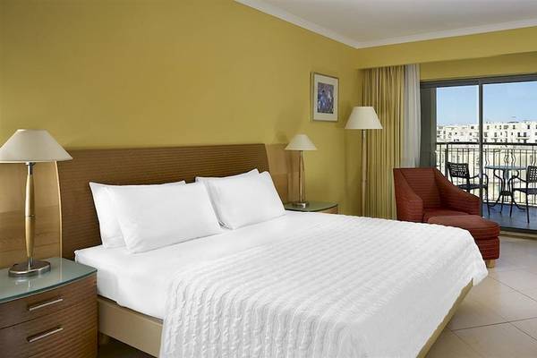 Hotelzimmer mit Balkon im Malta Marriott Hotel & Spa, mit gelben Wänden, bequemem Bett und Ausblick auf die Stadt.