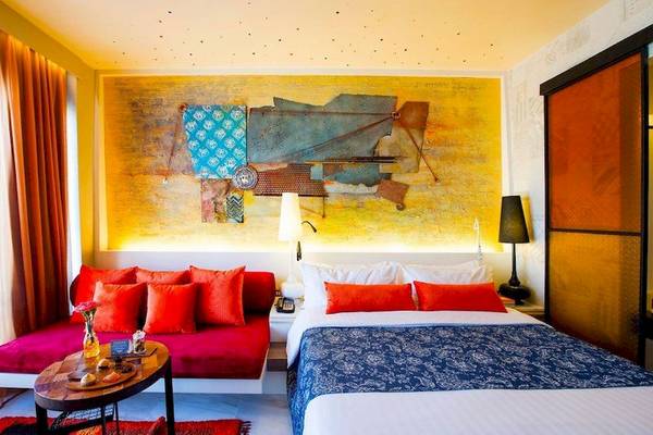 Innenansicht eines Zimmers im Siam@Siam Design Hotel Bangkok mit farbenfrohem Wandbild, rotem Sofa und Bett.